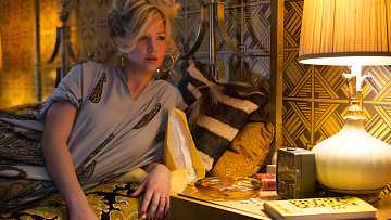 Žena ležící na posteli v ložnici s nočním stolkem plným předmětů